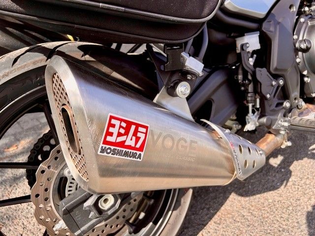 Yoshimura-Auspuff an einem Motorrad mit rot-weißem Branding. Der Auspuff ist silberfarben und hat ein perforiertes Ende.