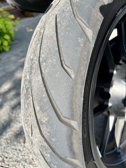 Nahaufnahme eines abgenutzten Motorradreifens, auf der Profilverschleiß und Rad zu sehen sind.