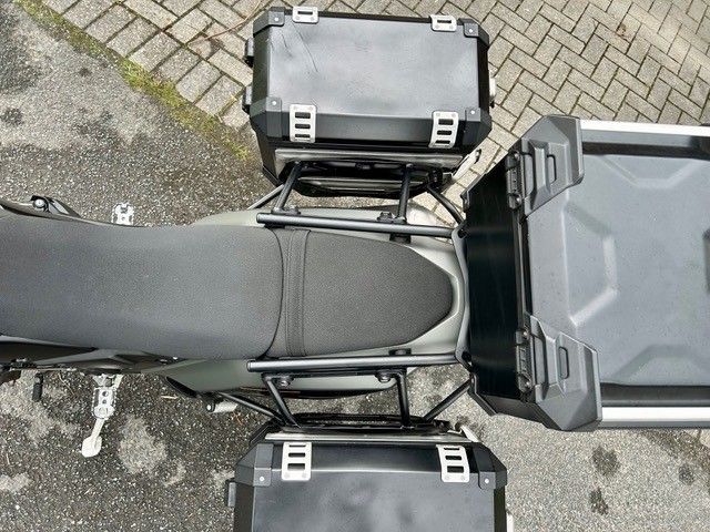 Draufsicht auf ein graues Motorrad mit Seitenkoffern, das auf einer gepflasterten Straße geparkt ist.