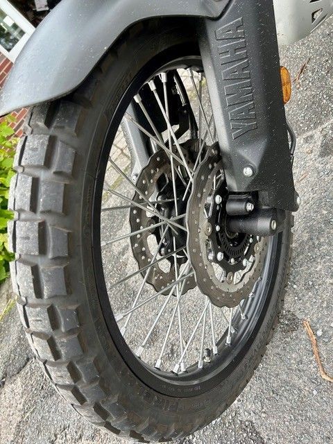 Nahaufnahme eines Motorradvorderrads mit schwarzem Reifen, Chromspeichen und grauem Schutzblech auf Asphalt