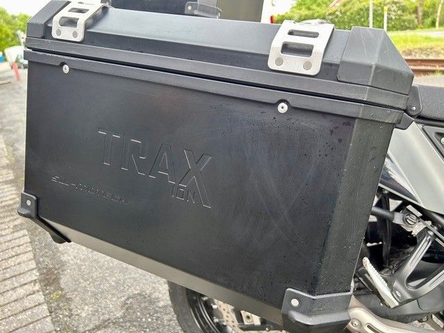Schwarzer TRAX Motorrad-Seitenkoffer mit silbernen Verschlüssen, montiert an einem Motorrad im Freien
