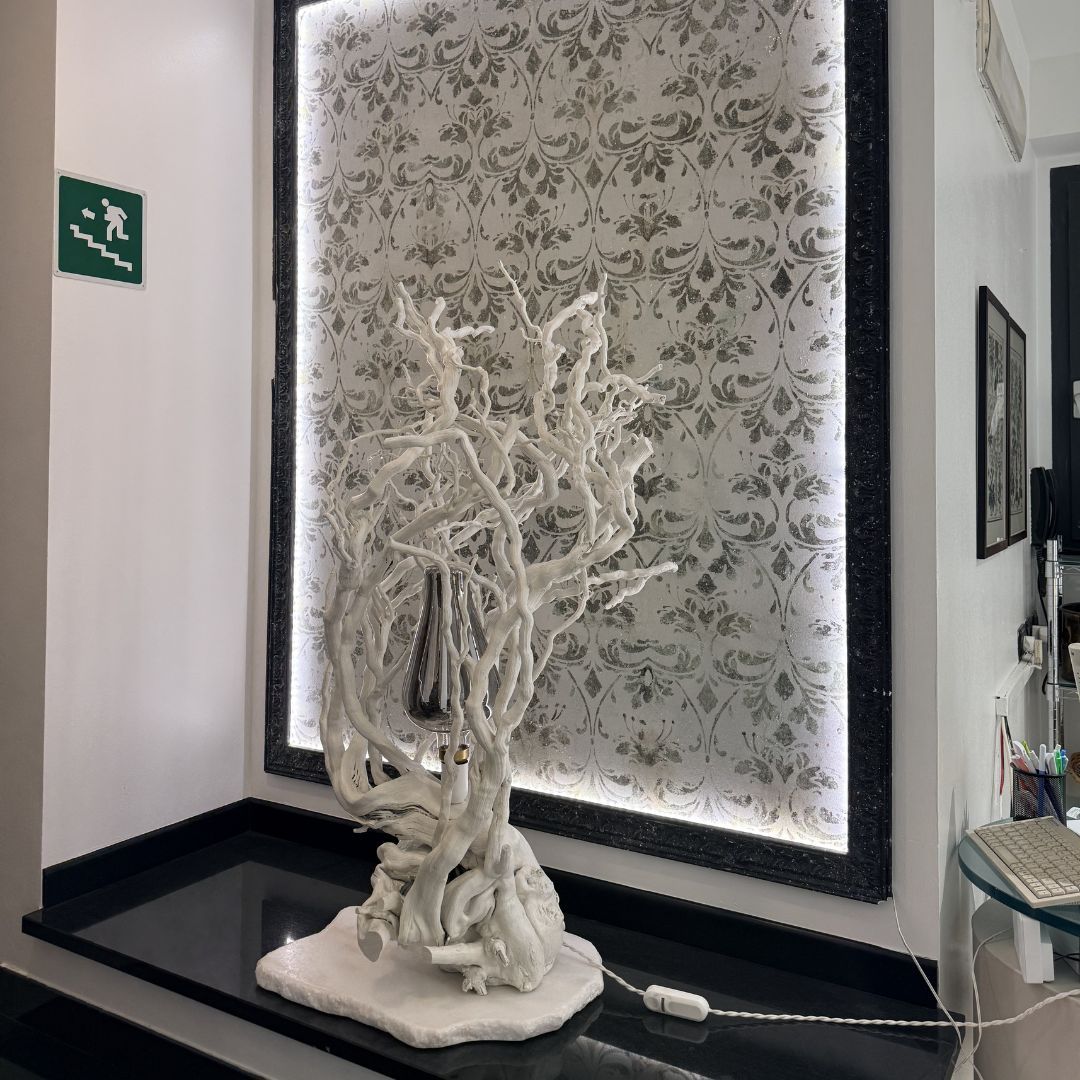 Scultura di ramo bianco su cornice nera, su sfondo di carta da parati floreale con cornice nera retroilluminata.