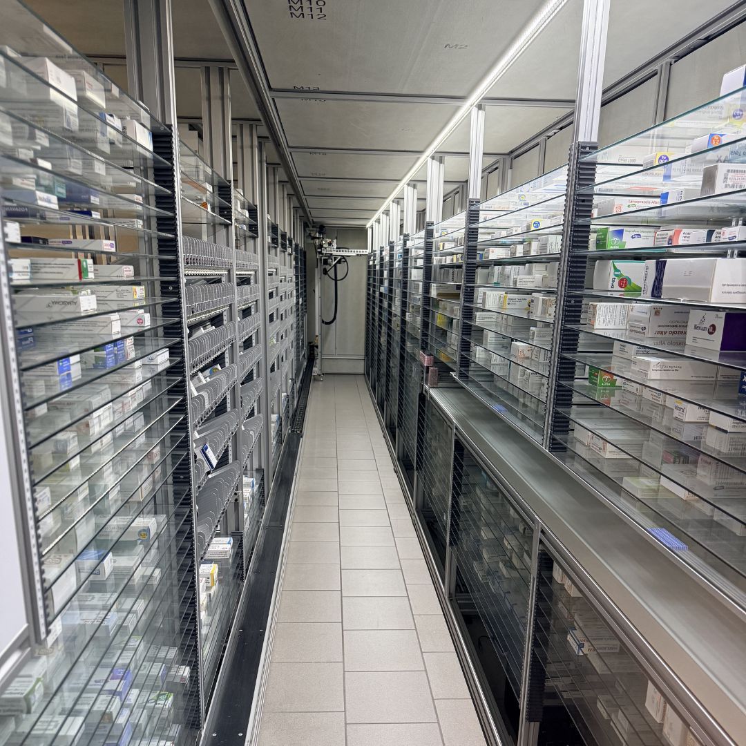 Corridoio stretto in un'area di stoccaggio di una farmacia con scaffali pieni di medicinali.