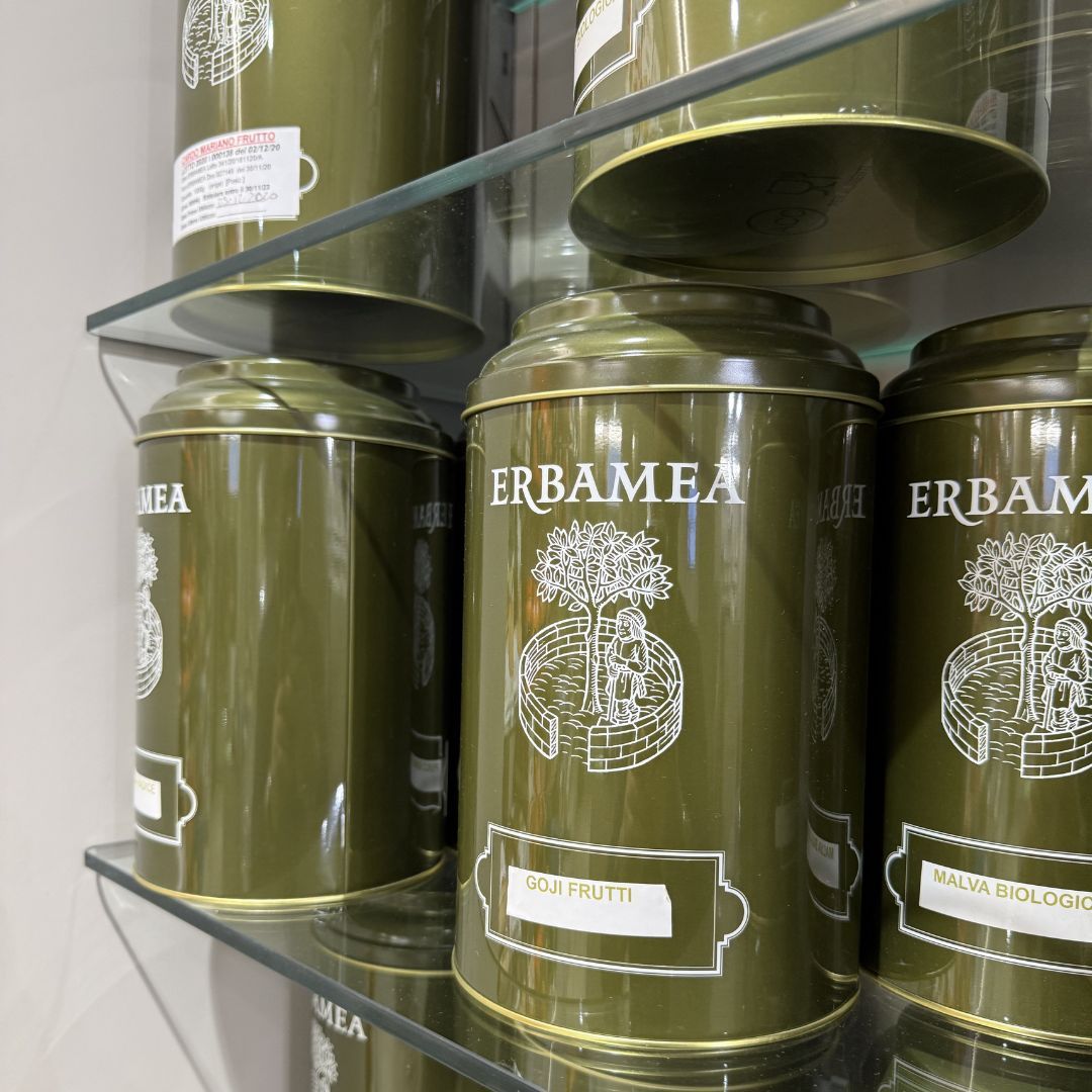 Lattine di tè Erba Mea verde oliva su ripiani in vetro, etichetta bianca con testo.