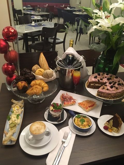 Mesa preparada con comida y bebida en un restaurante. Incluye pasteles, pastel, capuchino y flores.