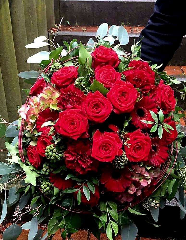 Auf einem Tisch steht ein Strauß roter Rosen und Grünpflanzen.