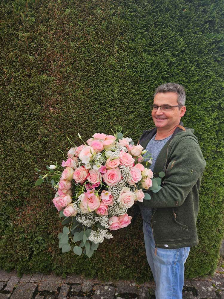 Ein Mann hält einen großen Strauß rosa Rosen.