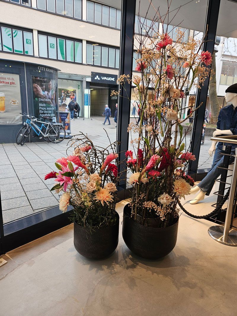 Zwei mit Blumen gefüllte Vasen stehen auf einem Tisch vor einem Fenster.