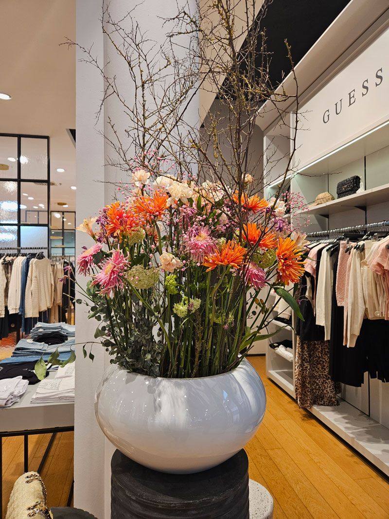 In einem Geschäft steht eine weiße Vase voller Blumen.