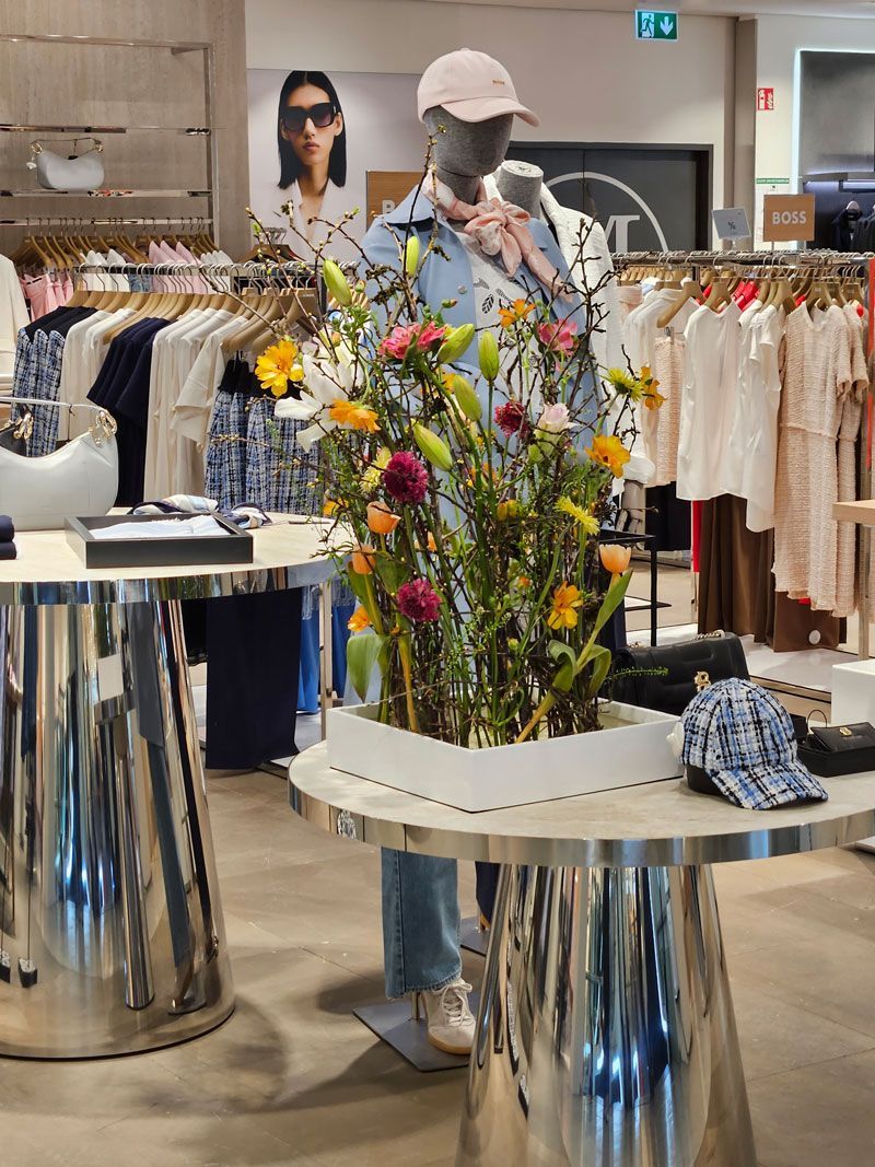 In einem Geschäft steht eine Schaufensterpuppe neben einem Tisch mit Blumen darauf.