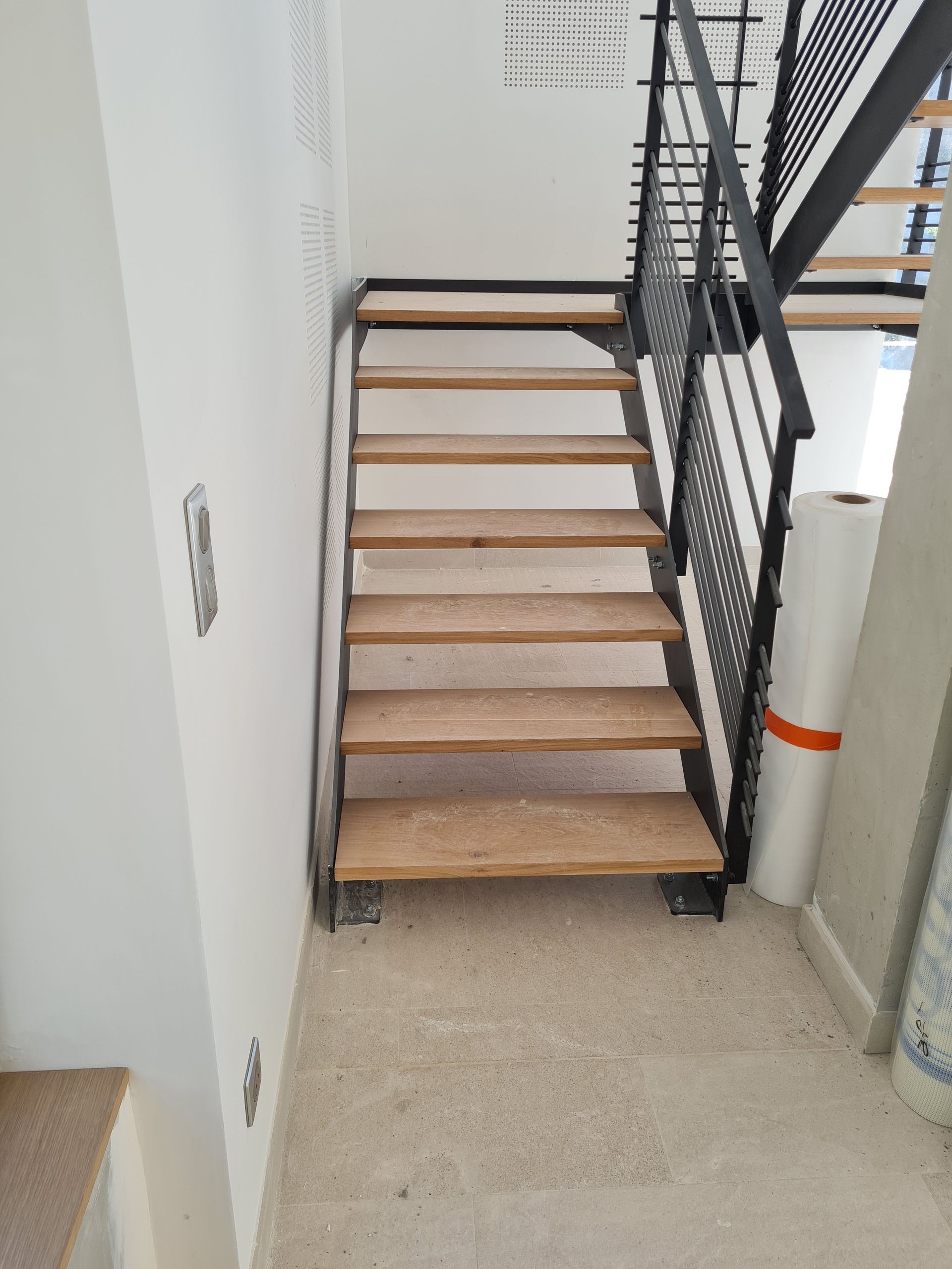 Escalier intérieur avec marches beiges et rampe noire dans un couloir étroit