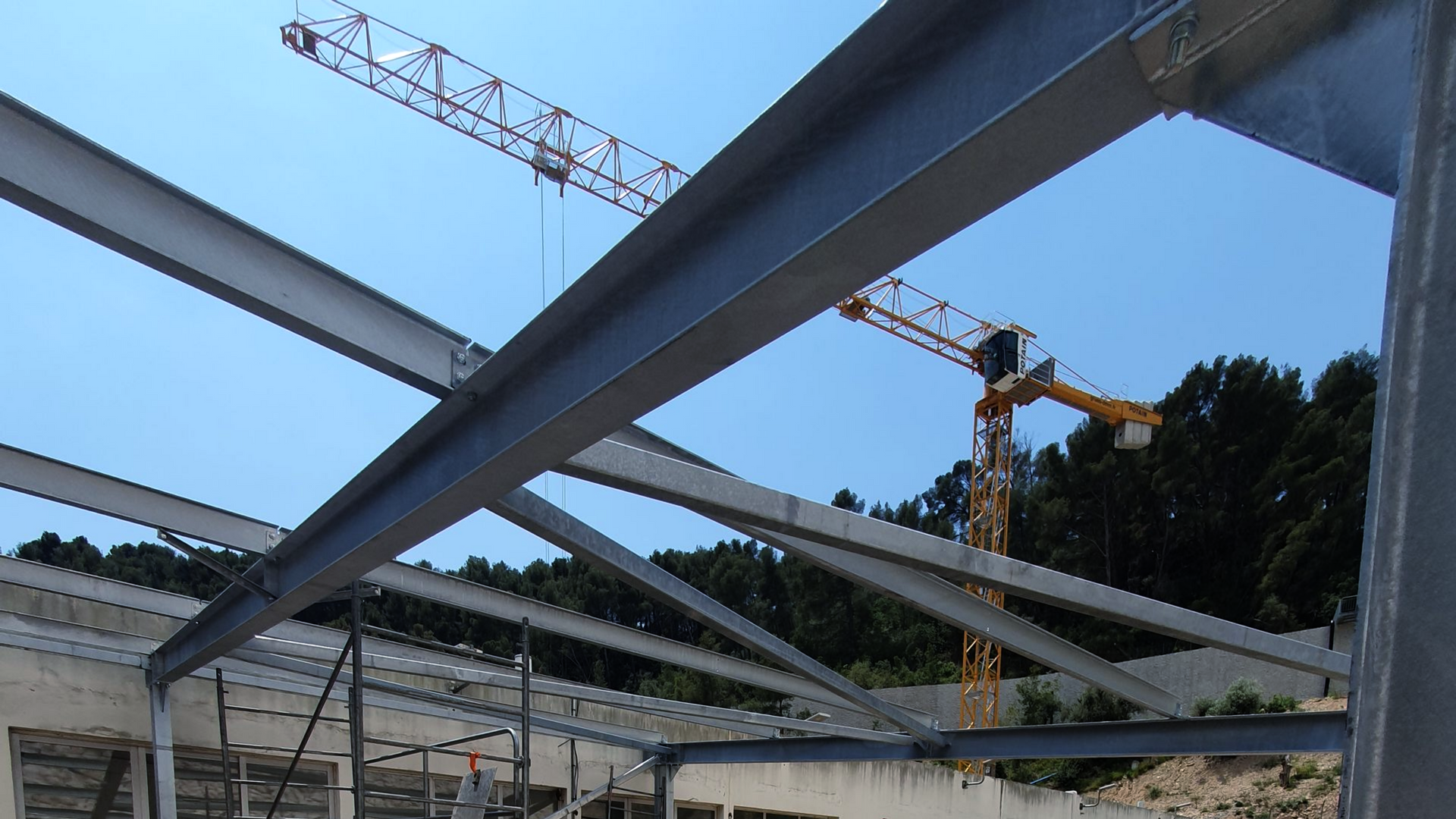 Poutres d'acier d'une structure de bâtiment en construction, avec des grues au-dessus, sur fond de ciel bleu.