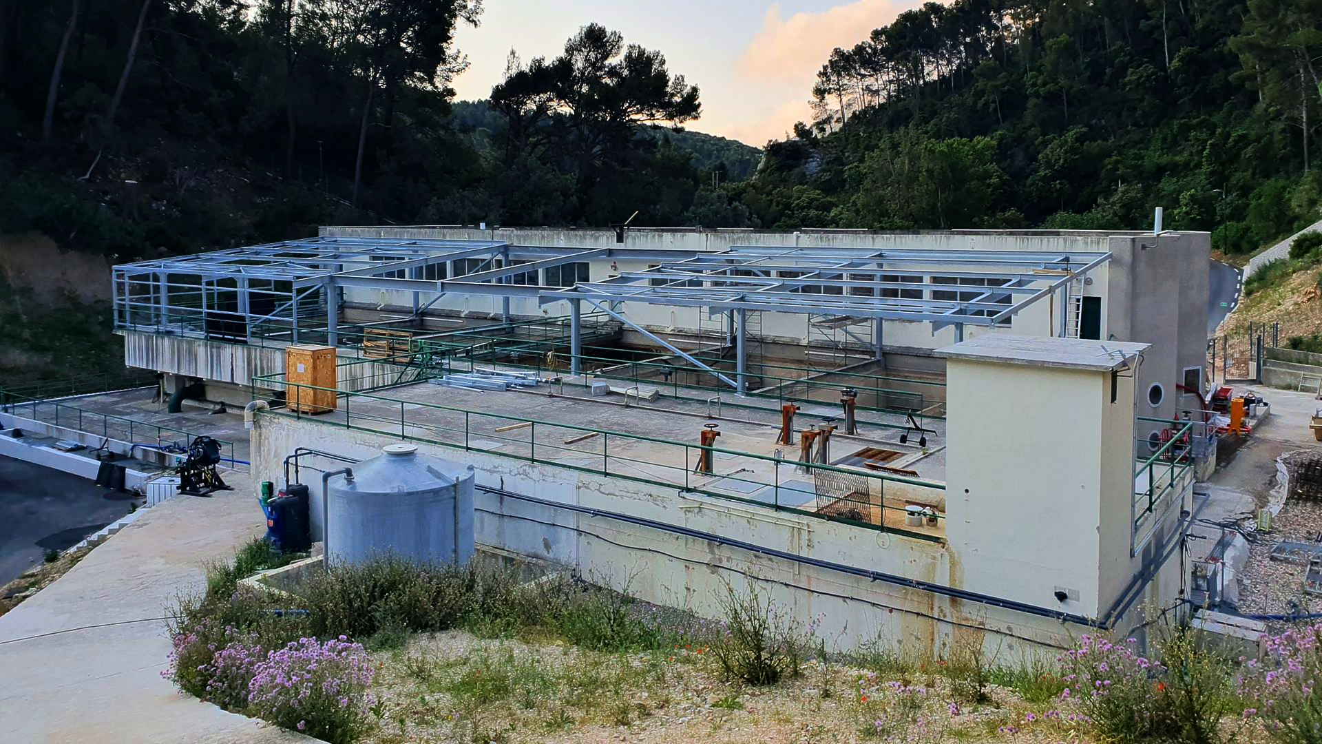 Chantier de construction avec structure métallique, ouvriers et fondations en béton au crépuscule