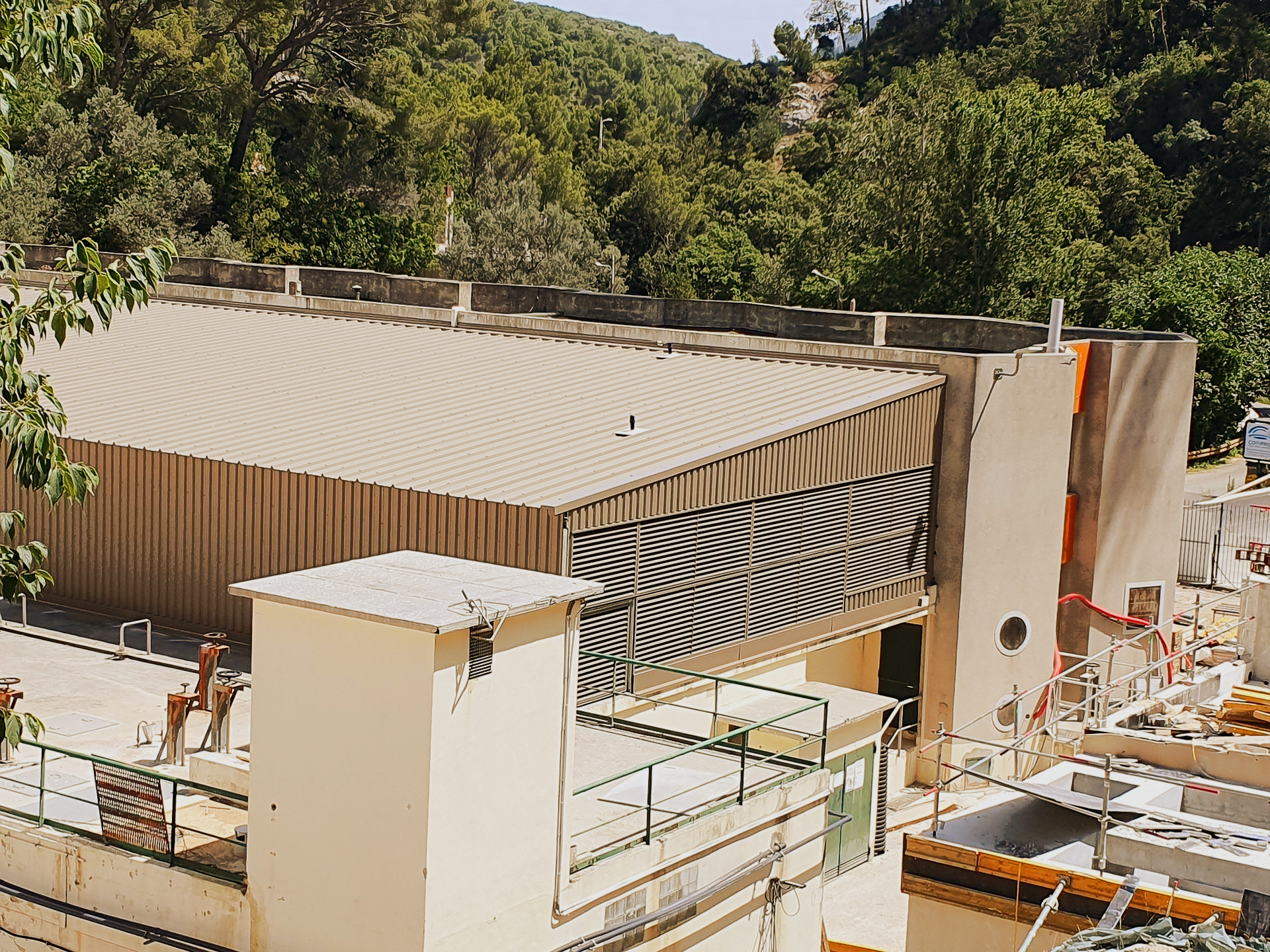 Terrasse sur le toit et toit en tôle ondulée à côté d'un bâtiment, avec des arbres et des collines en arrière-plan.