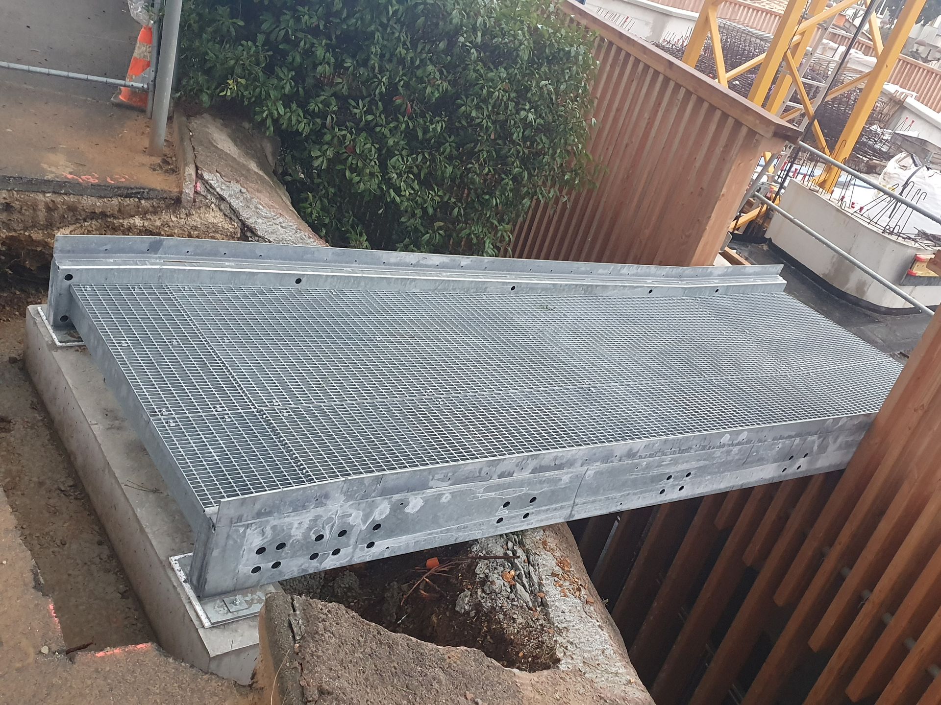 Plateforme ou rampe en métal galvanisé reposant au-dessus d'un petit espace à côté d'une clôture et de buissons.