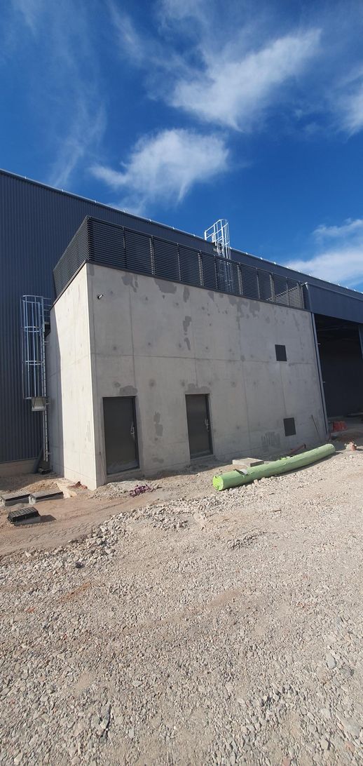 Bâtiment en béton à côté d’un terrain en gravier sous un ciel bleu éclatant.