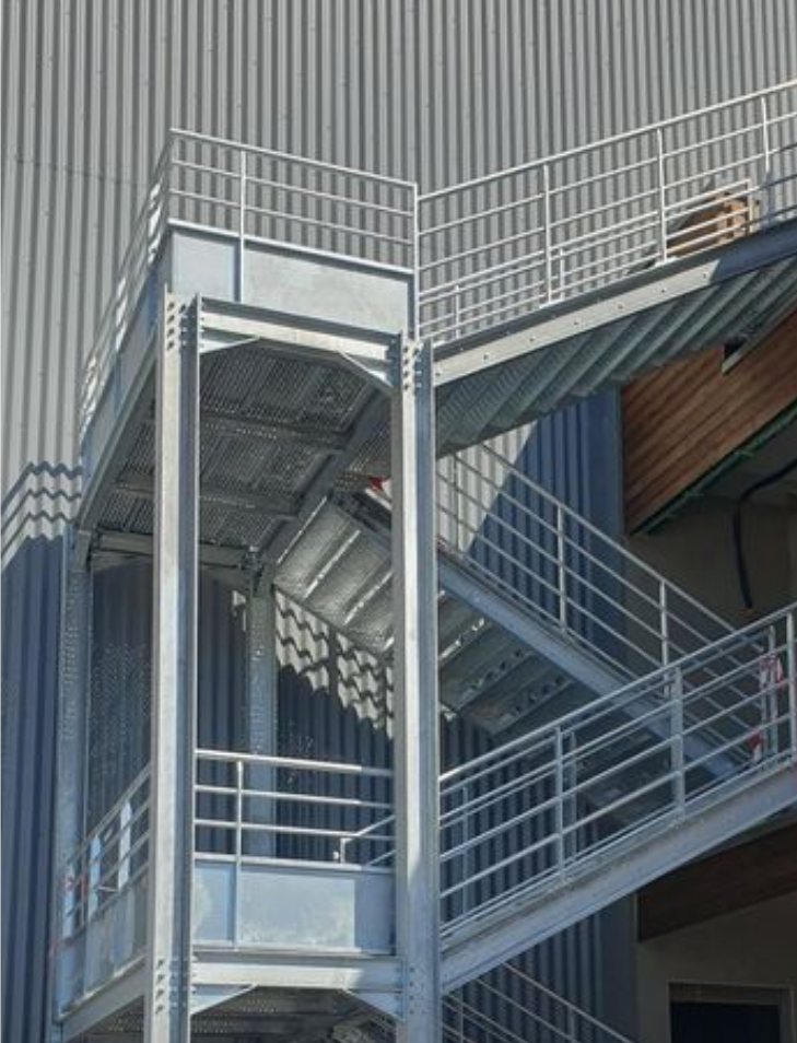 Escalier extérieur en métal avec rampes et paliers bleu-gris sur une façade de bâtiment