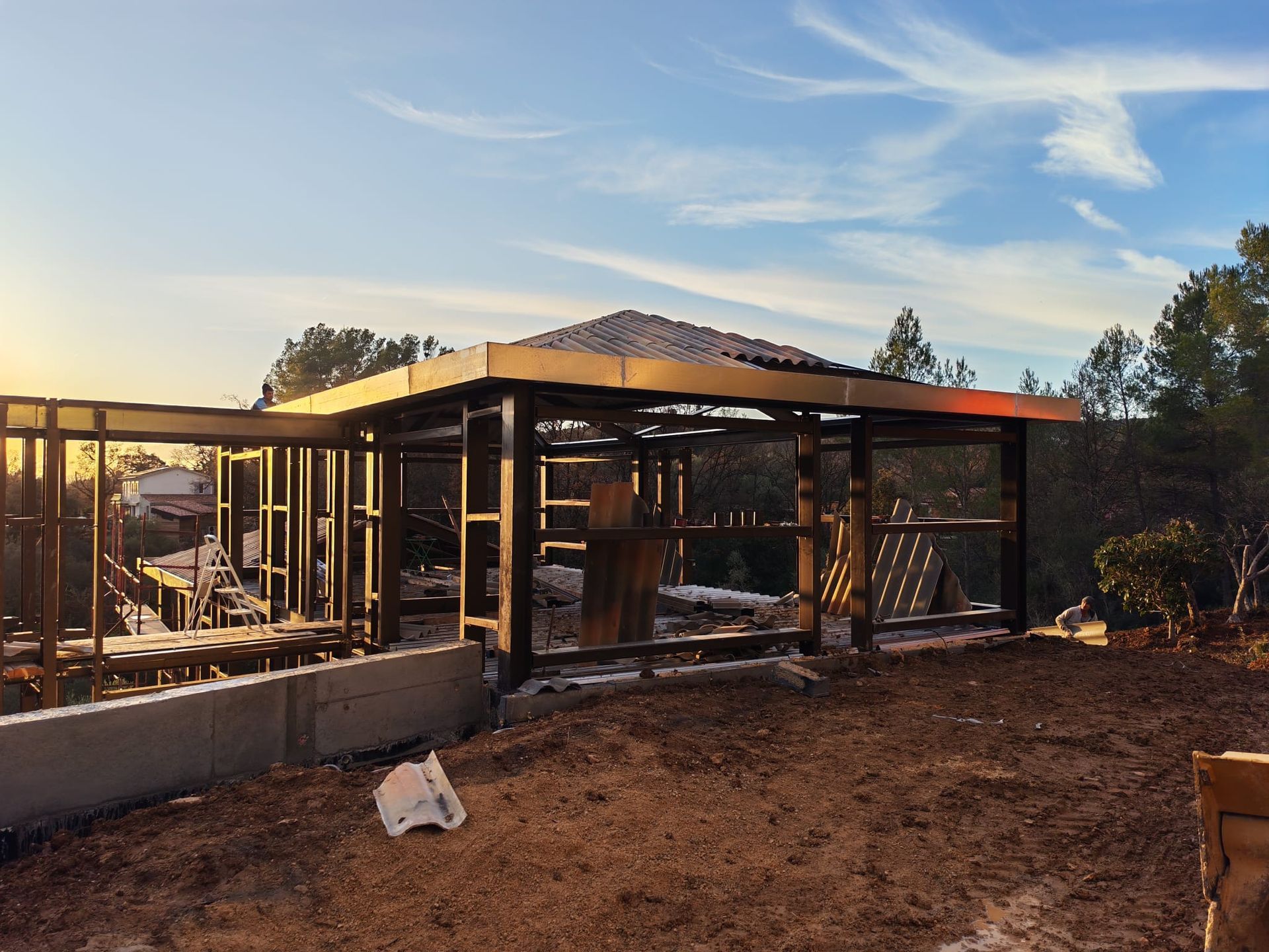 Maison en construction, partiellement à ossature en bois, au coucher du soleil, avec murs et charpente apparents.