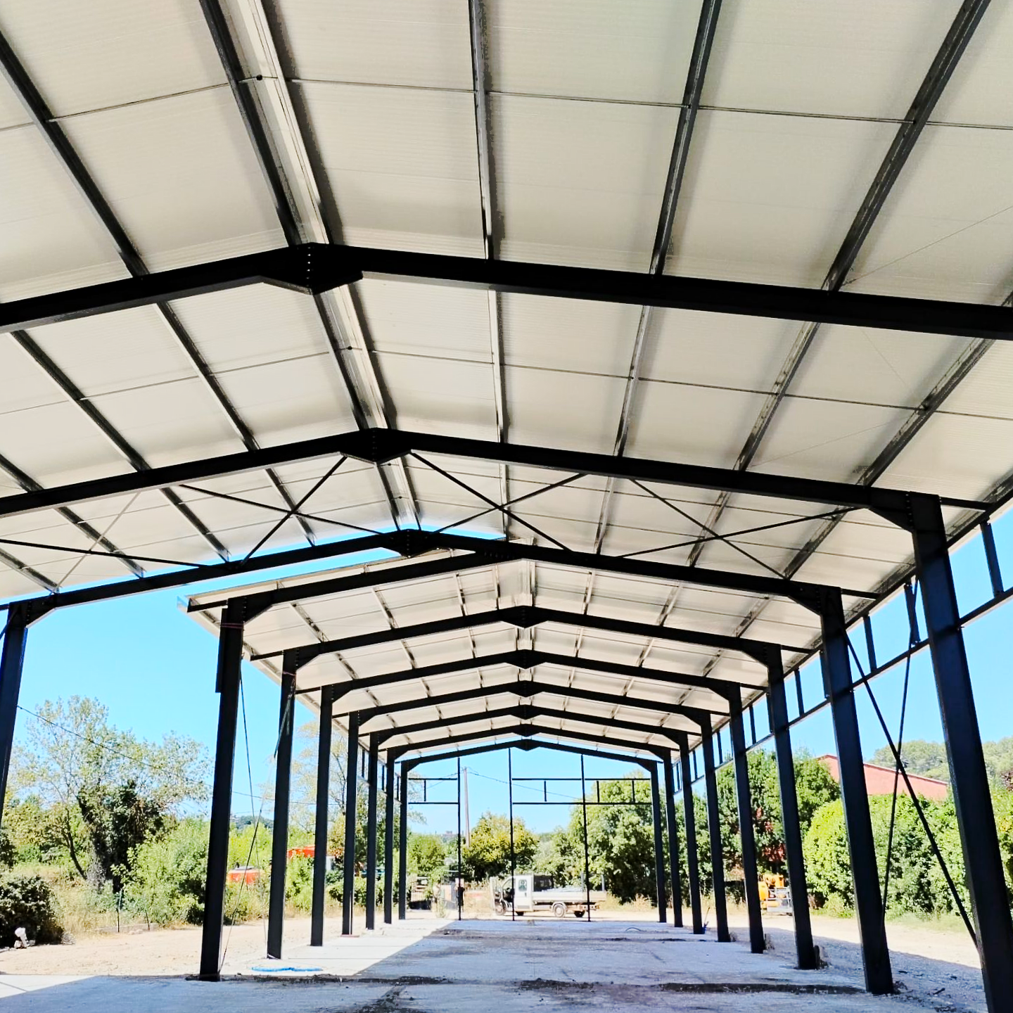 Pavillon extérieur couvert avec une canopée blanche et une structure métallique noire, ouvert sur les arbres et le ciel bleu