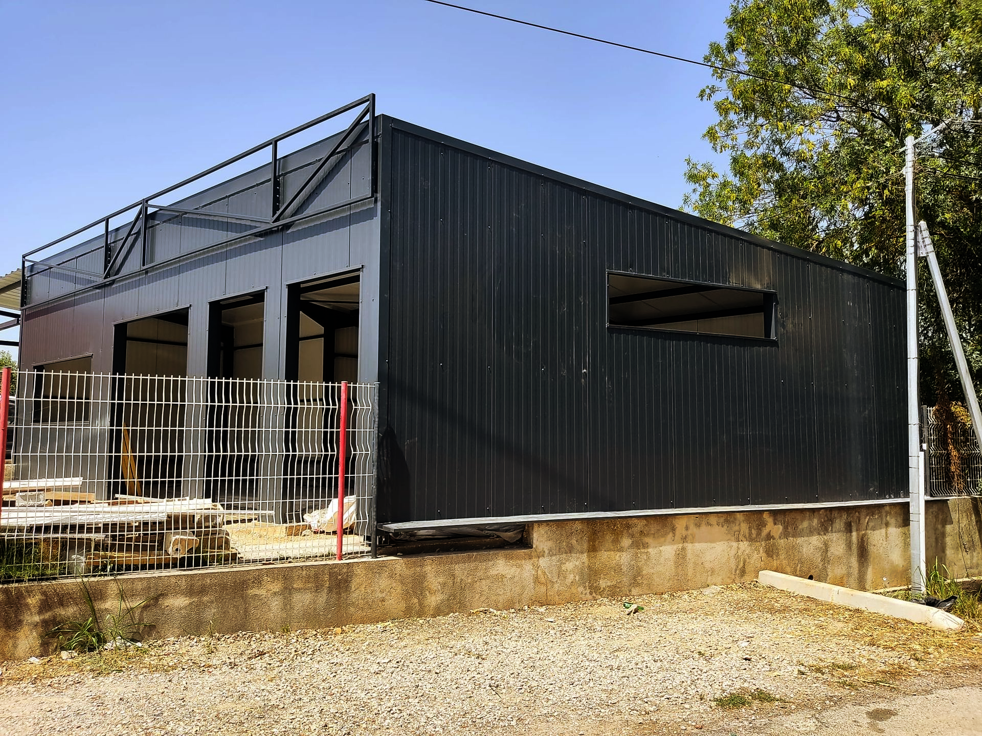 Bâtiment moderne en métal noir en construction, avec une terrasse sur le toit et un premier plan en gravier