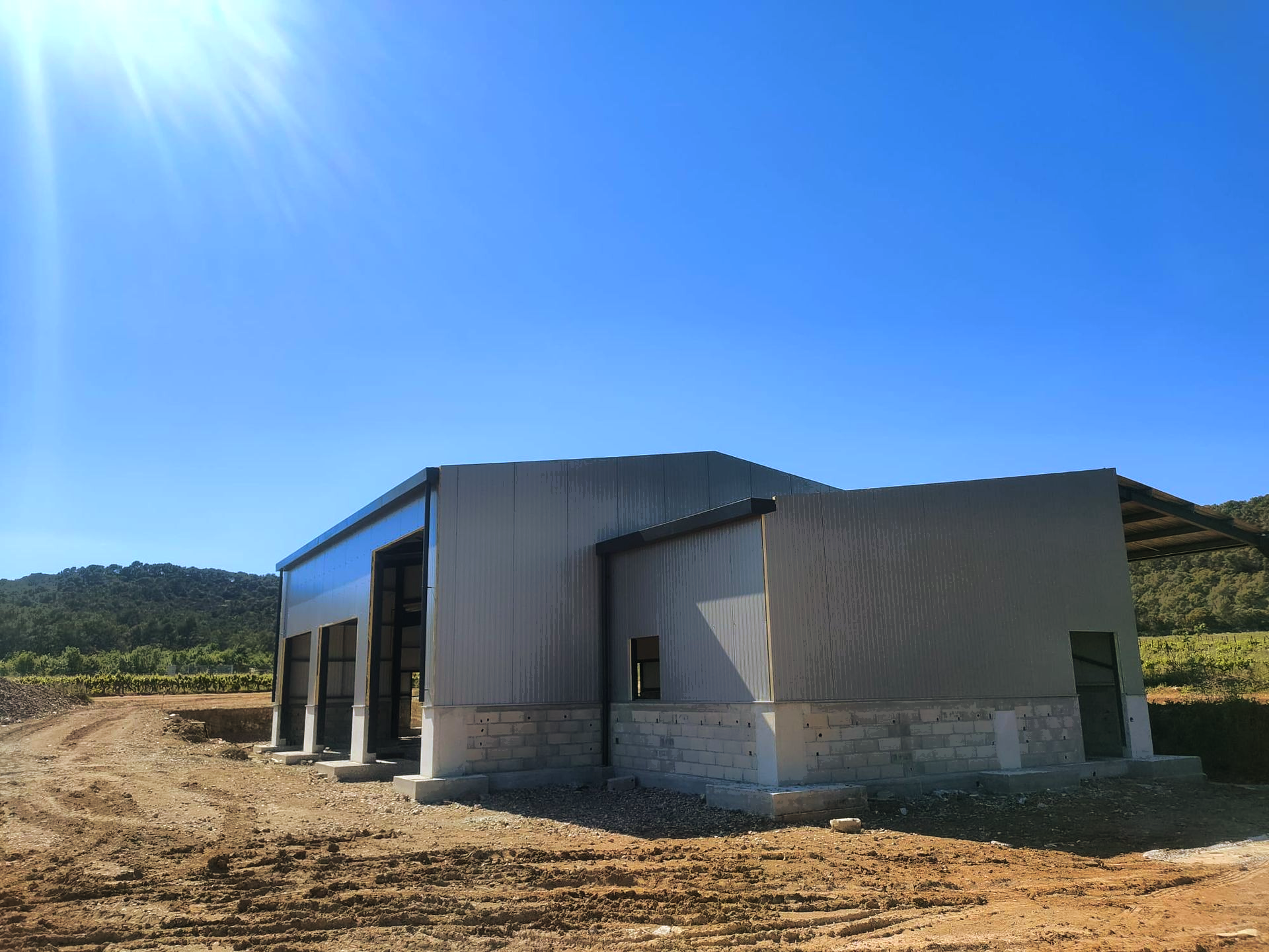 Maison avec bardage métallique en construction sur un terrain sec et aride sous un ciel d'un bleu éclatant