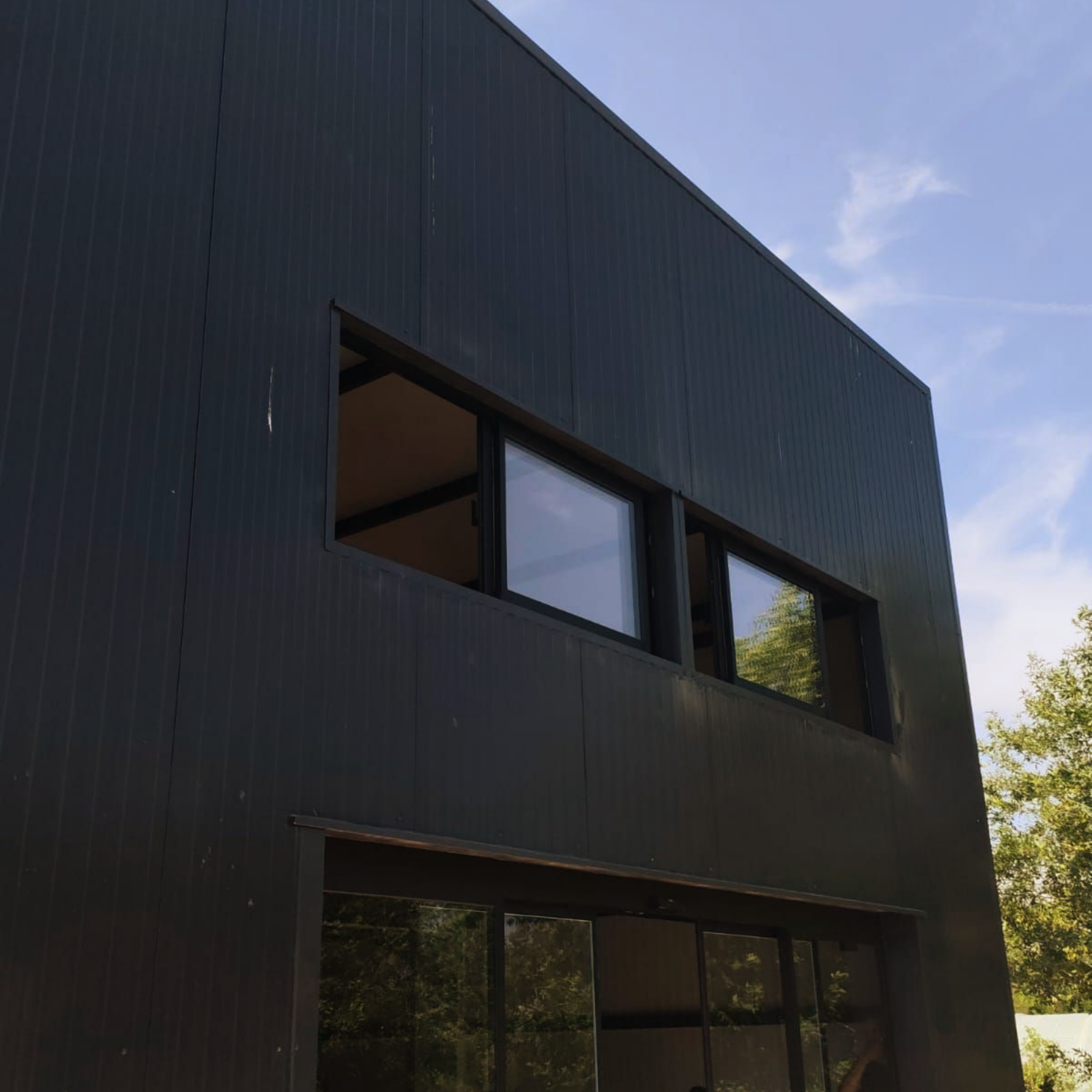 Extérieur d'une maison moderne noire à deux étages avec de grandes fenêtres et un toit en pente.