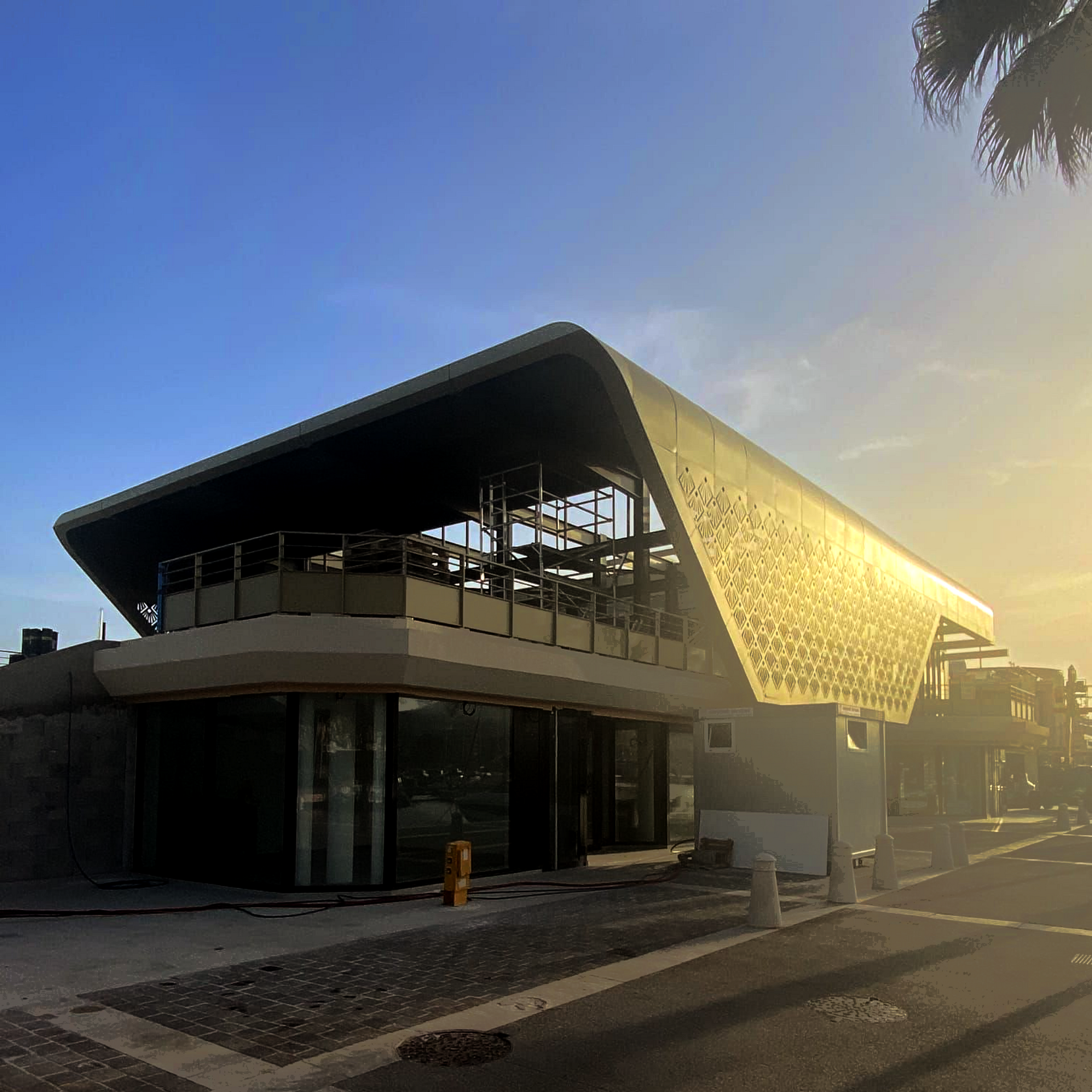 Bâtiment moderne au toit incurvé au coucher du soleil, façade de verre illuminée d'une lumière chaude.