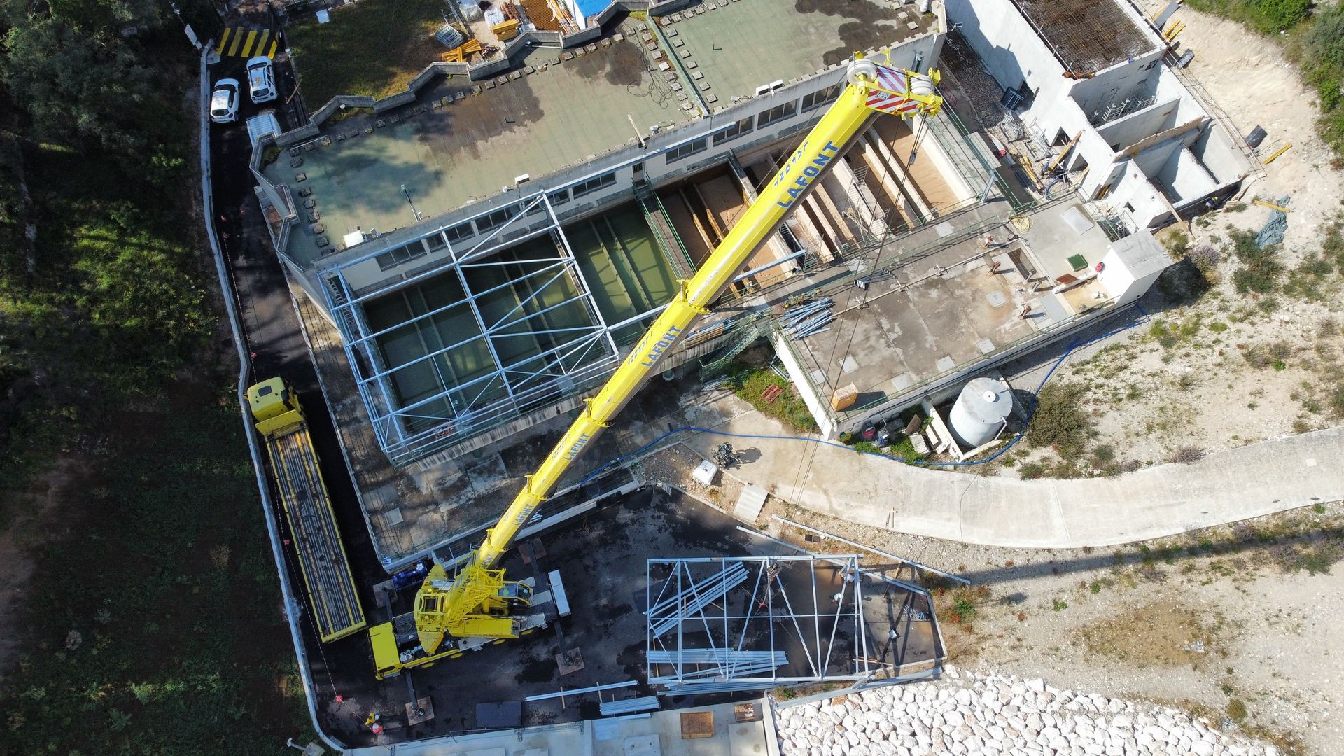 Vue aérienne d'un chantier de construction avec une grande grue jaune à côté d'une structure en construction.