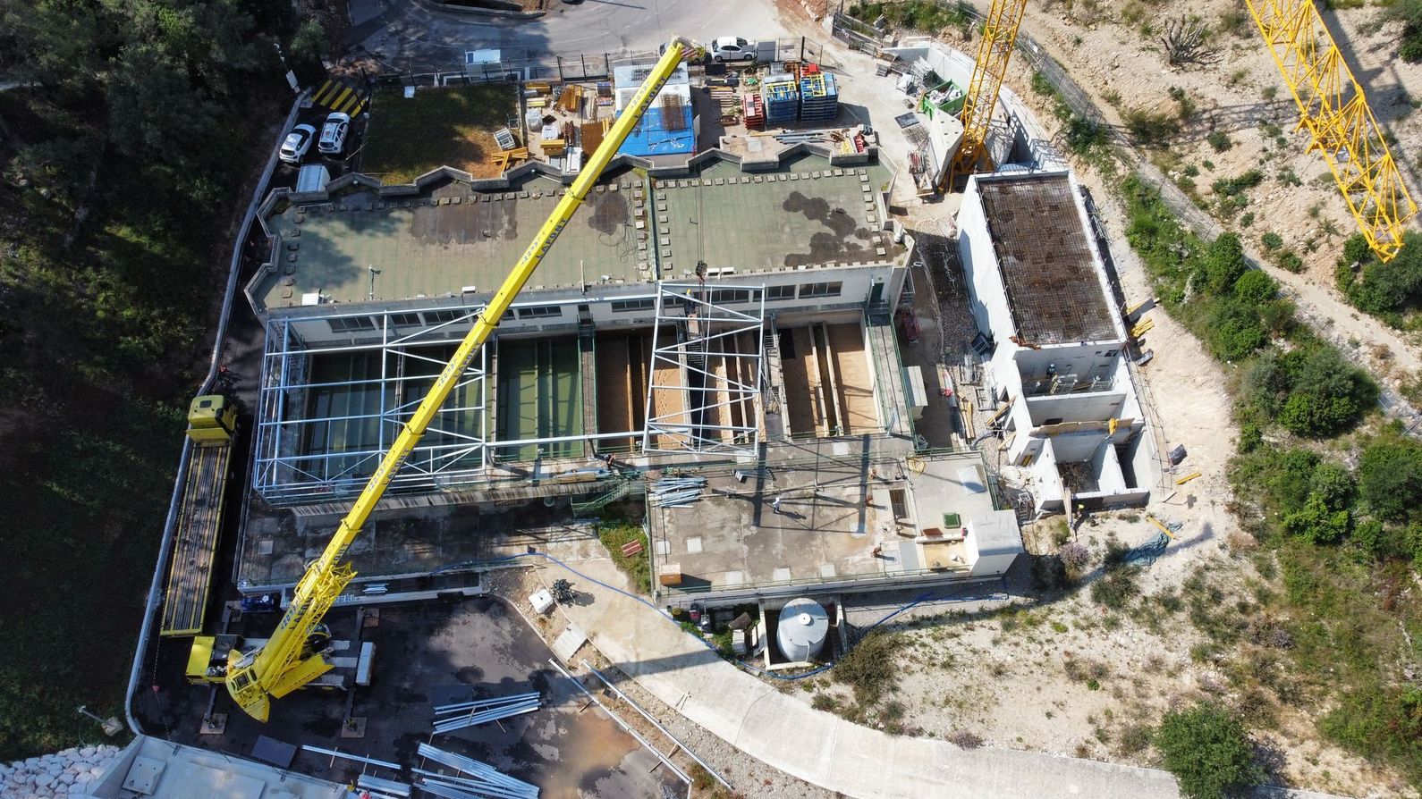 Vue aérienne d'un bâtiment endommagé avec une grue jaune et des débris éparpillés autour du site.