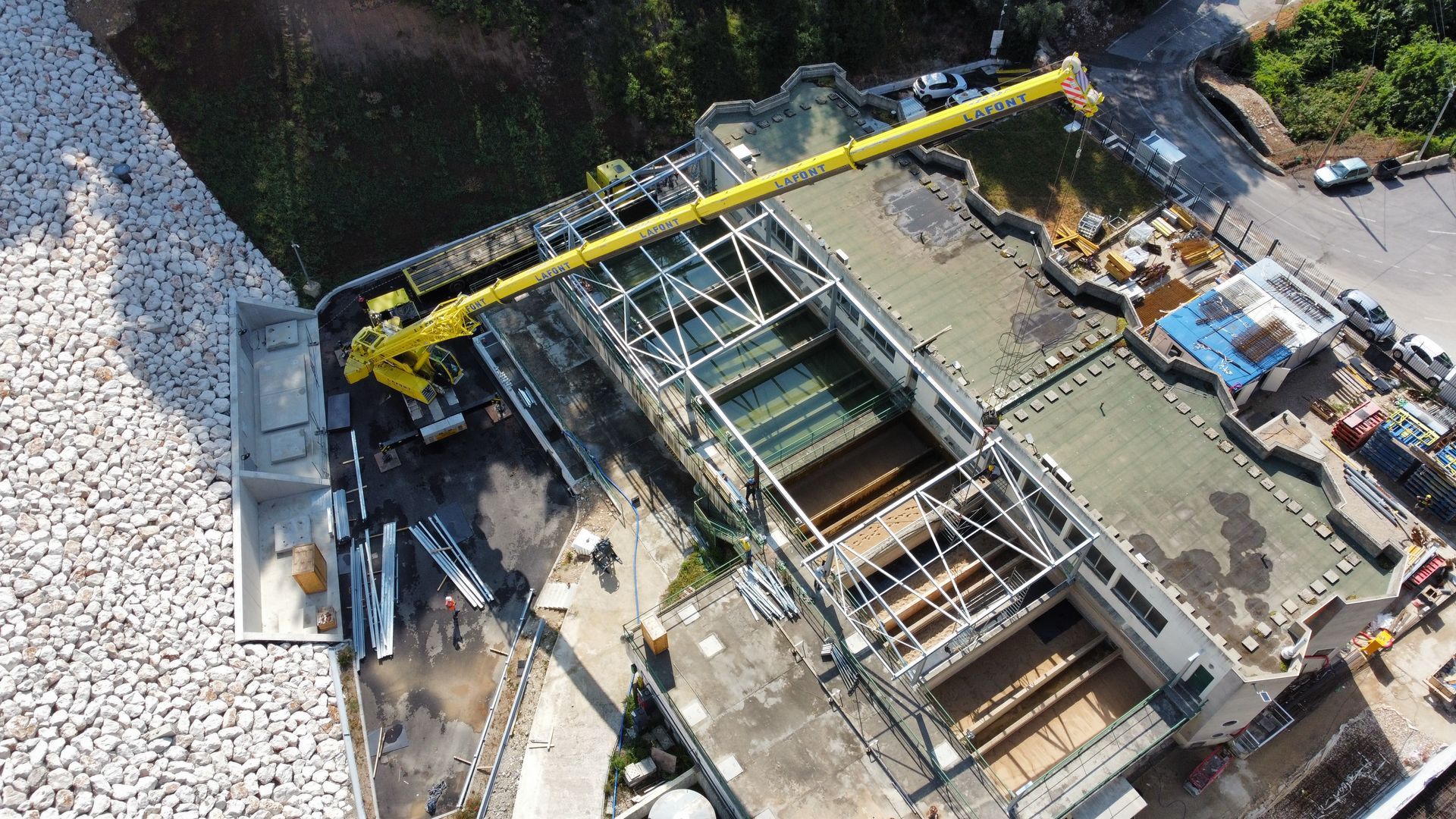 Vue aérienne d'une grue jaune en activité sur un chantier de construction au bord d'un rivage rocheux.