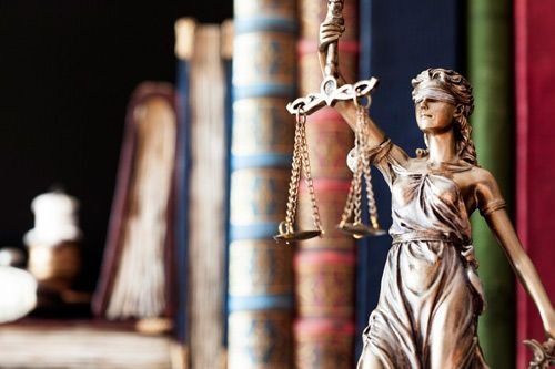 Una estatua de la justicia está parada frente a una fila de libros.