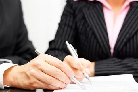 Un hombre y una mujer están sentados en una mesa escribiendo en un trozo de papel.