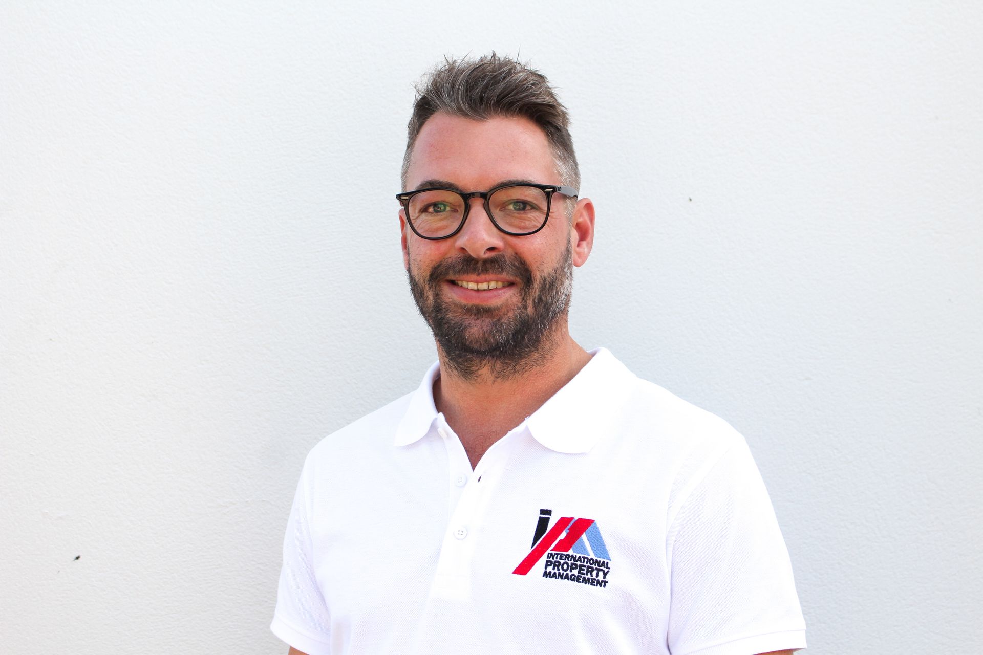 Un hombre con barba y gafas lleva un polo blanco.