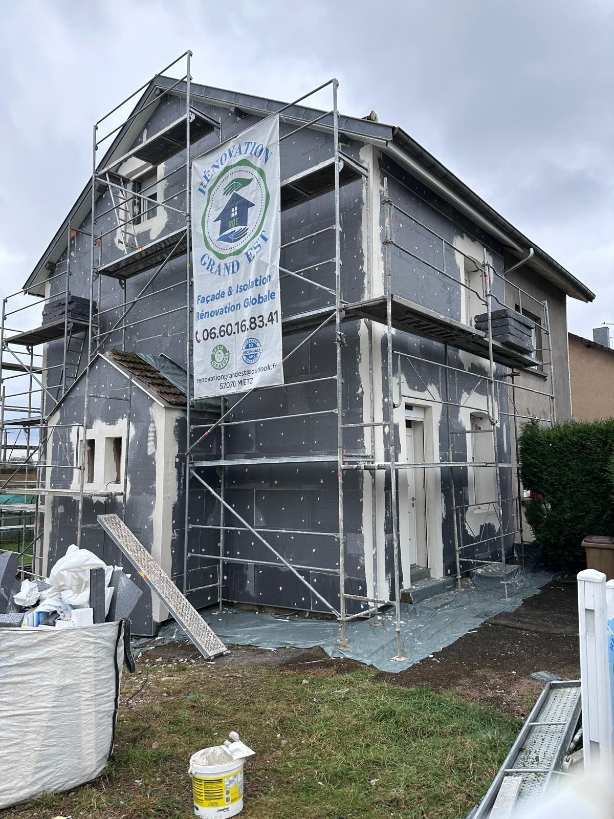 Extérieur de la maison en construction avec échafaudage ; panneaux isolants gris foncé visibles.
