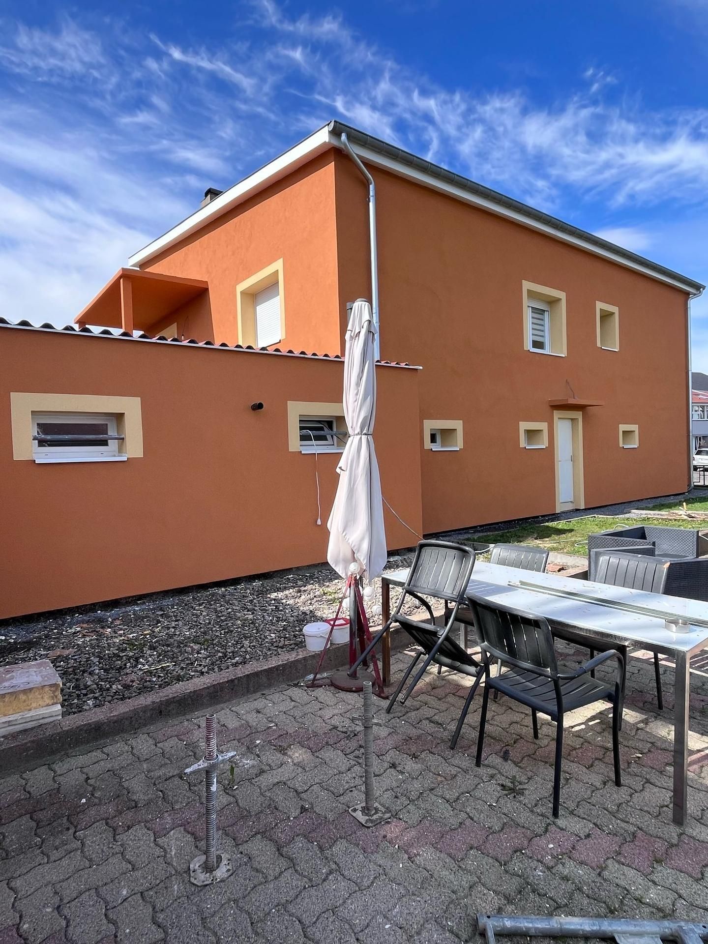 Bâtiment orange avec mobilier de jardin et parasol fermé par une journée ensoleillée.