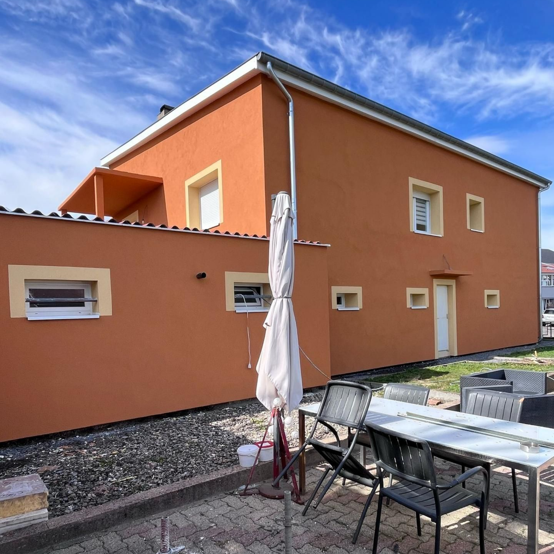 Maison orange à deux étages avec ensemble de salle à manger extérieur et parasol par une journée ensoleillée.