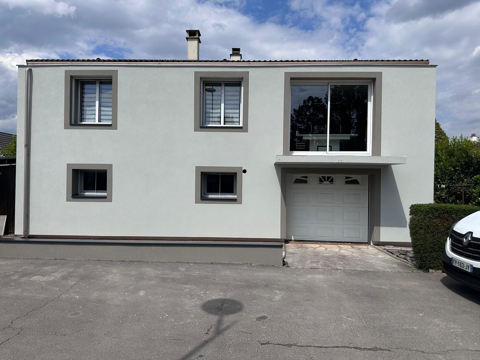 Maison à deux étages avec façade gris clair, fenêtres et porte de garage.