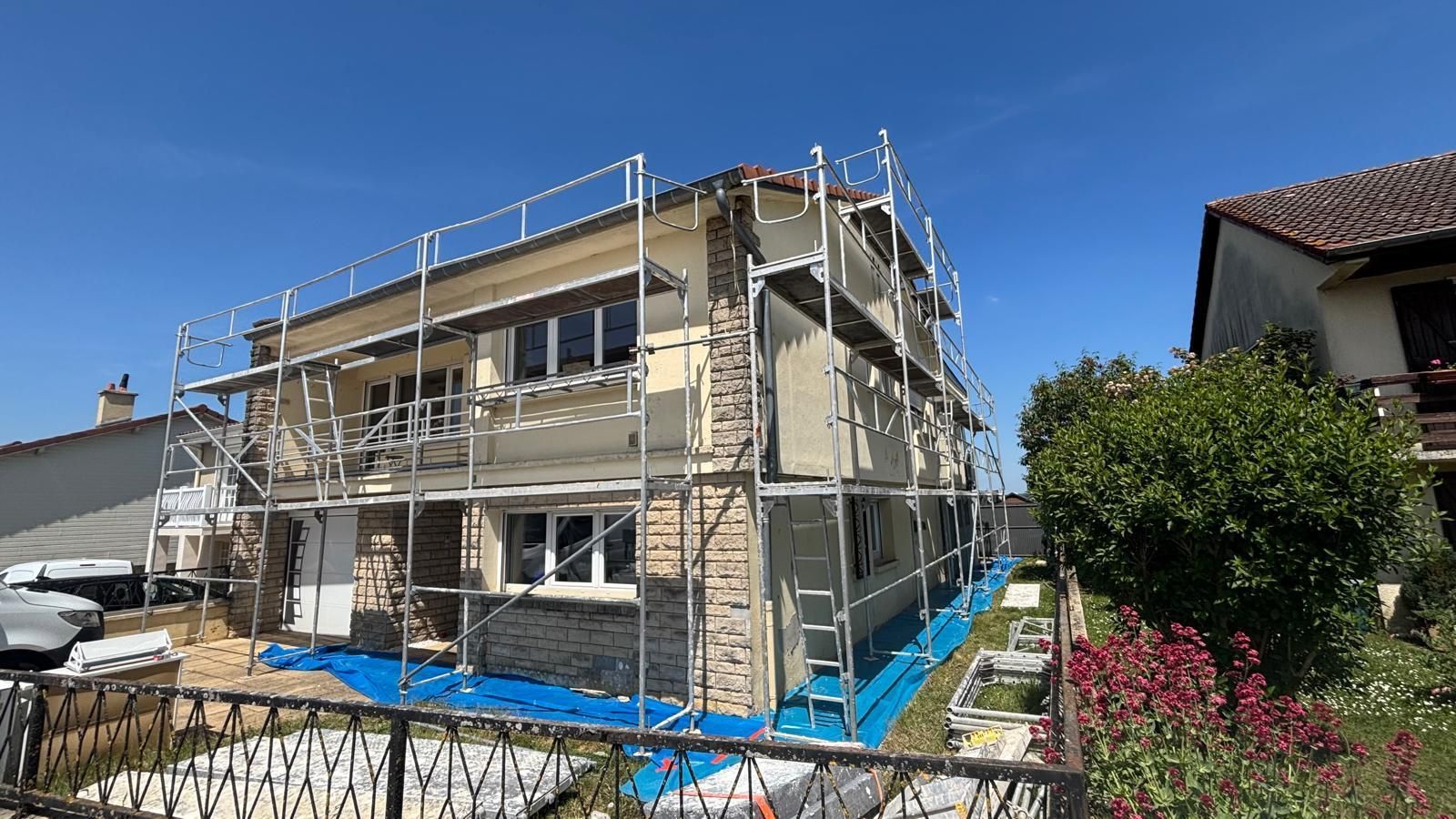 Extérieur de la maison en rénovation avec échafaudage, bâche bleue et façade en pierre.