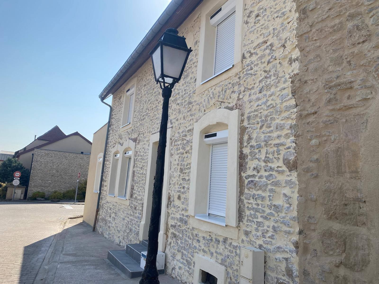 Bâtiment en pierre avec des volets blancs et un lampadaire noir par une journée ensoleillée.