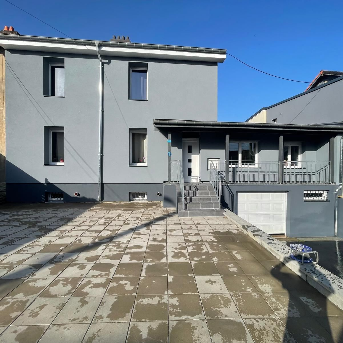 Maison grise à deux étages avec porche et allée.