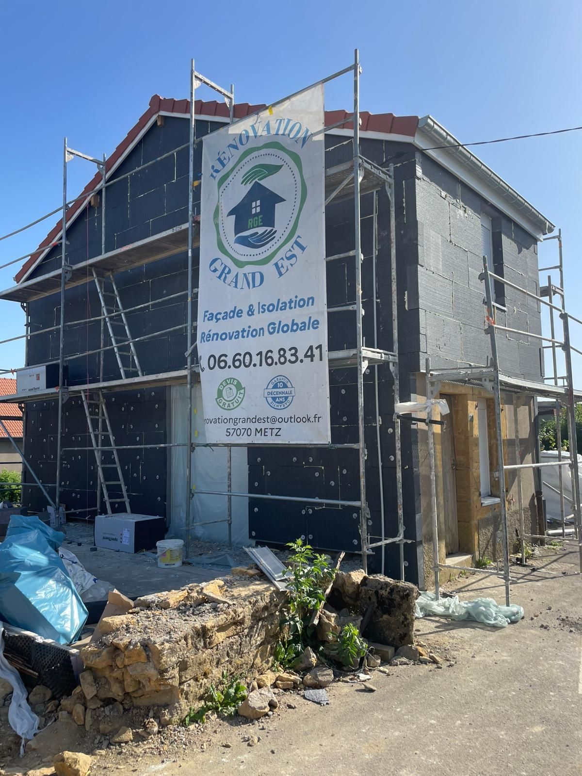 Extérieur de la maison en construction avec échafaudage ; panneaux isolants gris foncé visibles.