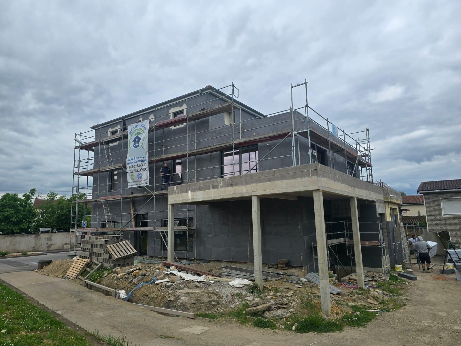 Chantier de construction avec échafaudage autour d'un bâtiment gris de deux étages en construction.