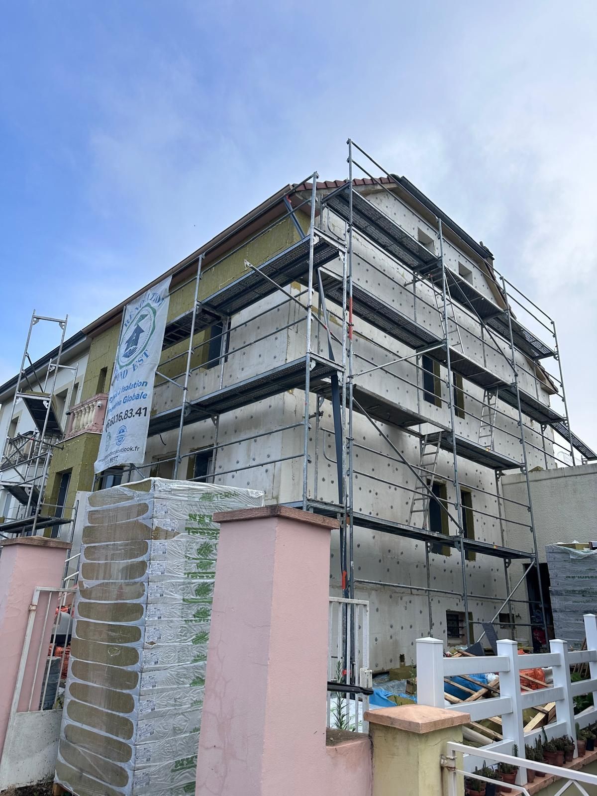 Bâtiment en construction avec échafaudage ; façade pâle, ciel bleu.
