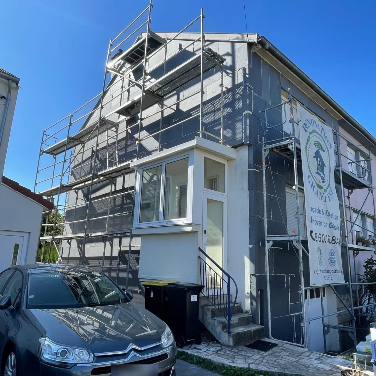 Extérieur du bâtiment en cours de rénovation avec échafaudage ; voiture garée devant.