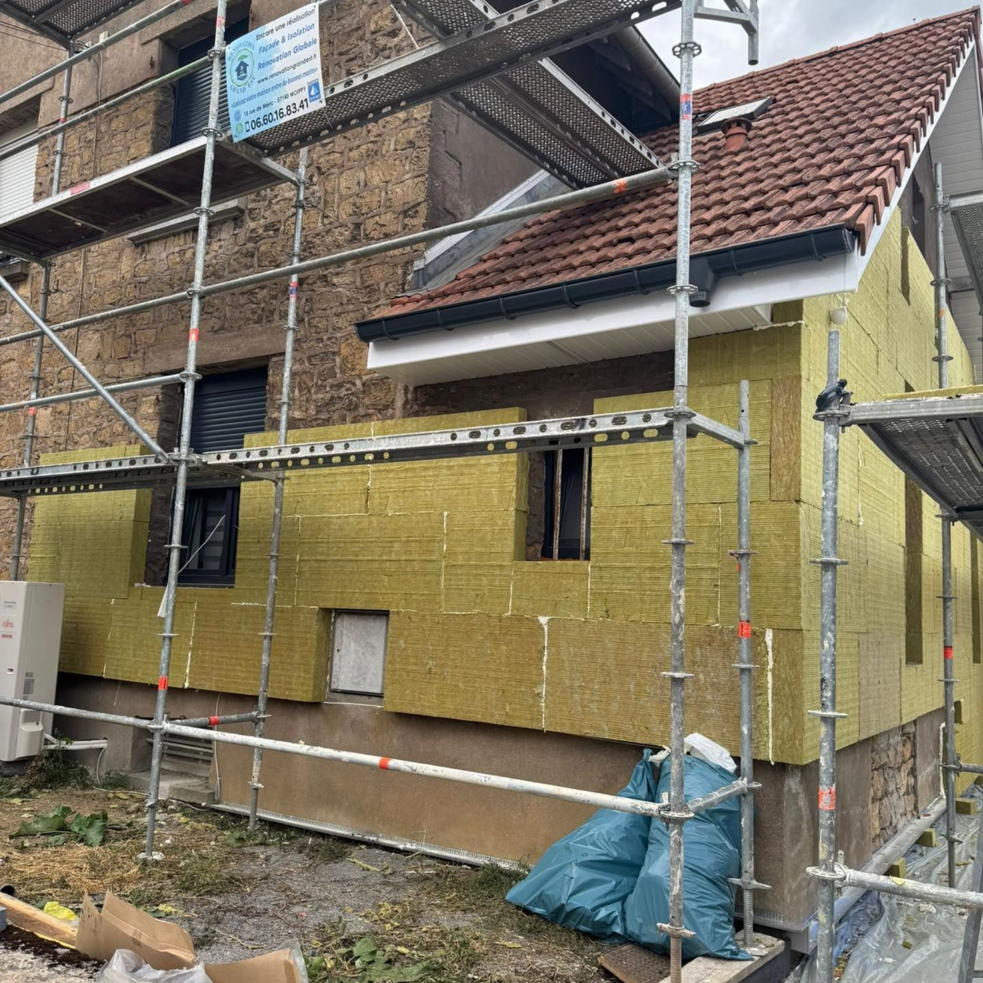 Rénovation extérieure maison : panneaux isolants posés, échafaudage, toiture en briques brunes, tuiles rouges.