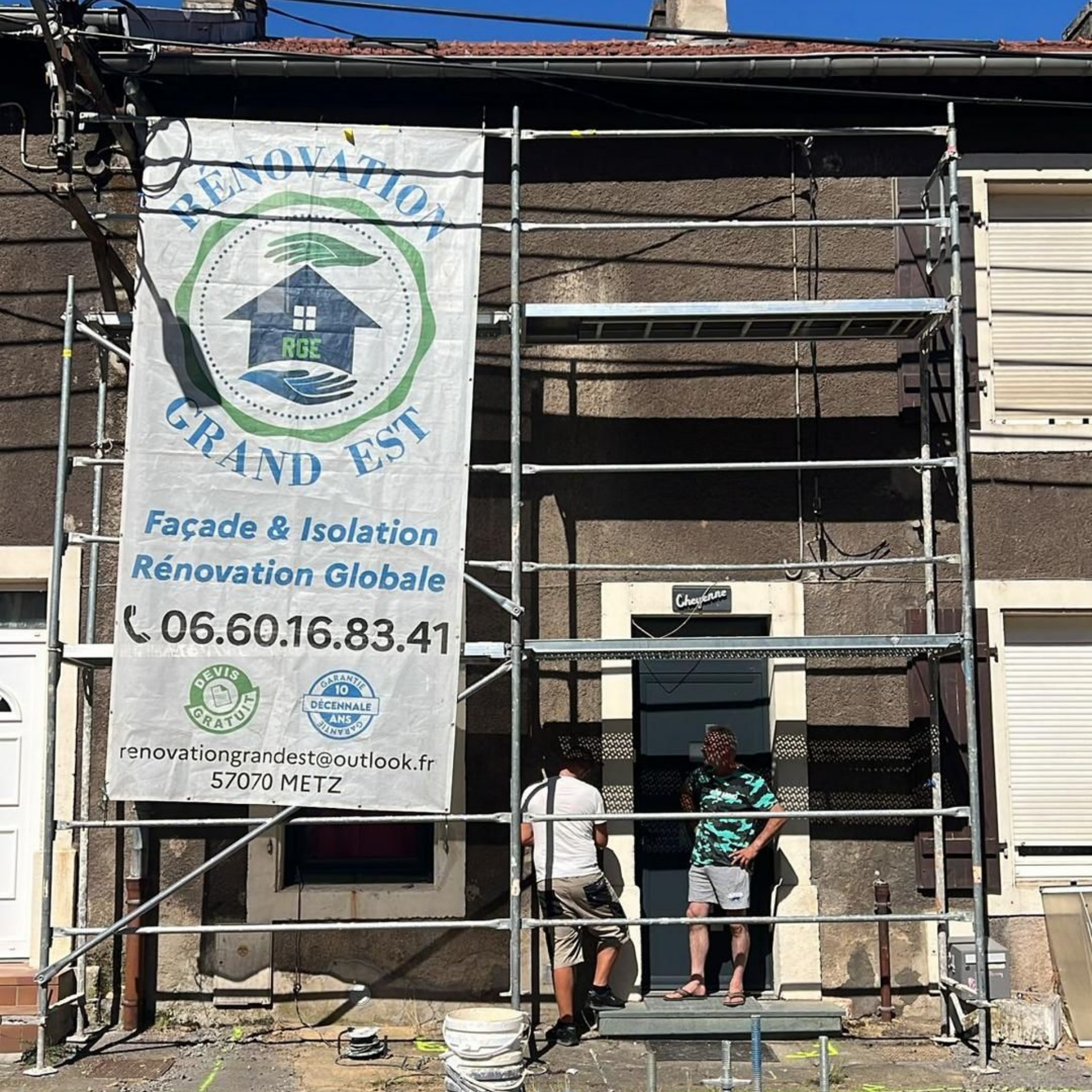 Des ouvriers sur un échafaudage rénovent la façade d'un bâtiment. La bannière indique Rénovation Grand Est.
