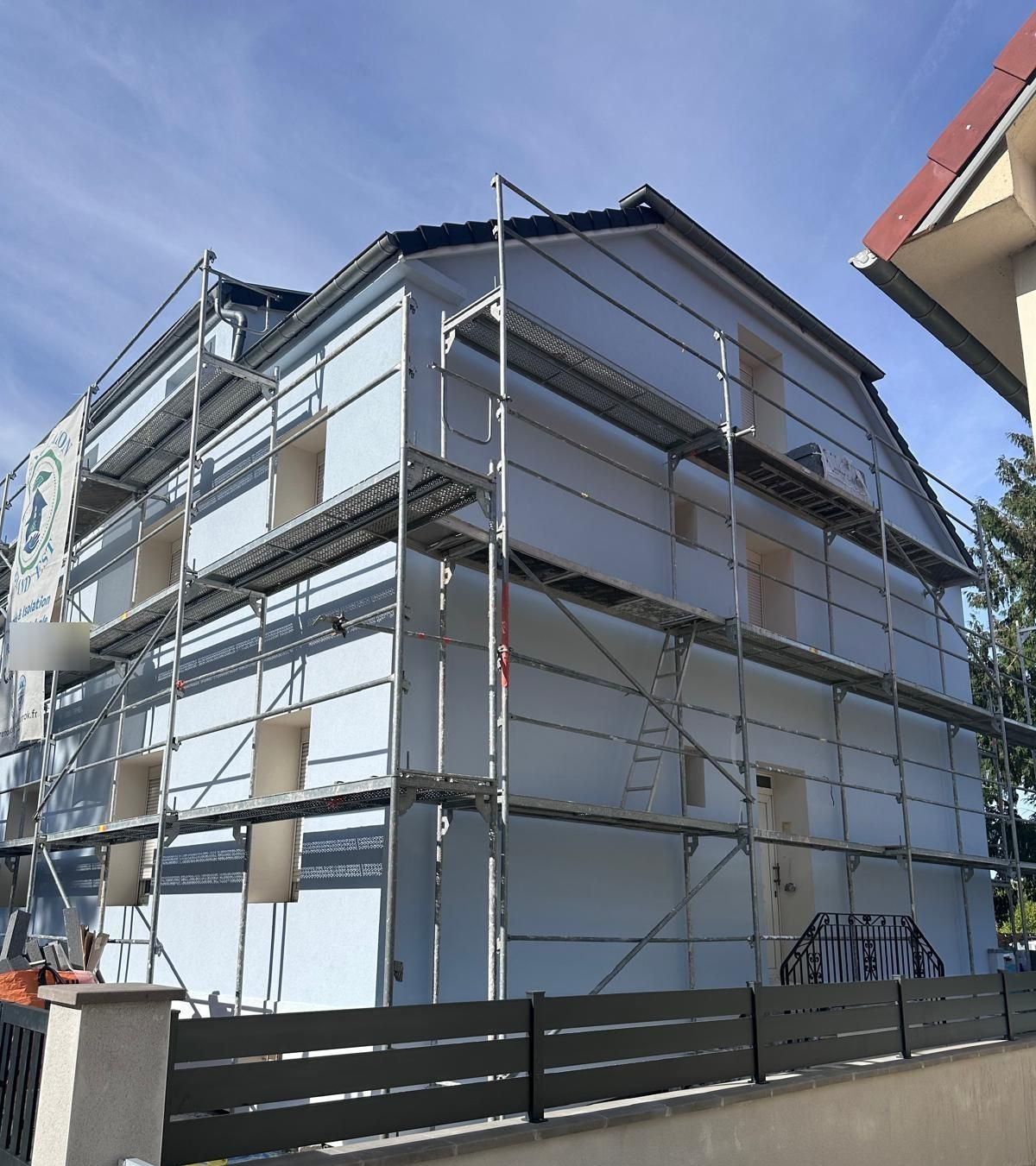 Extérieur du bâtiment en construction, recouvert d'isolant blanc, avec échafaudage.