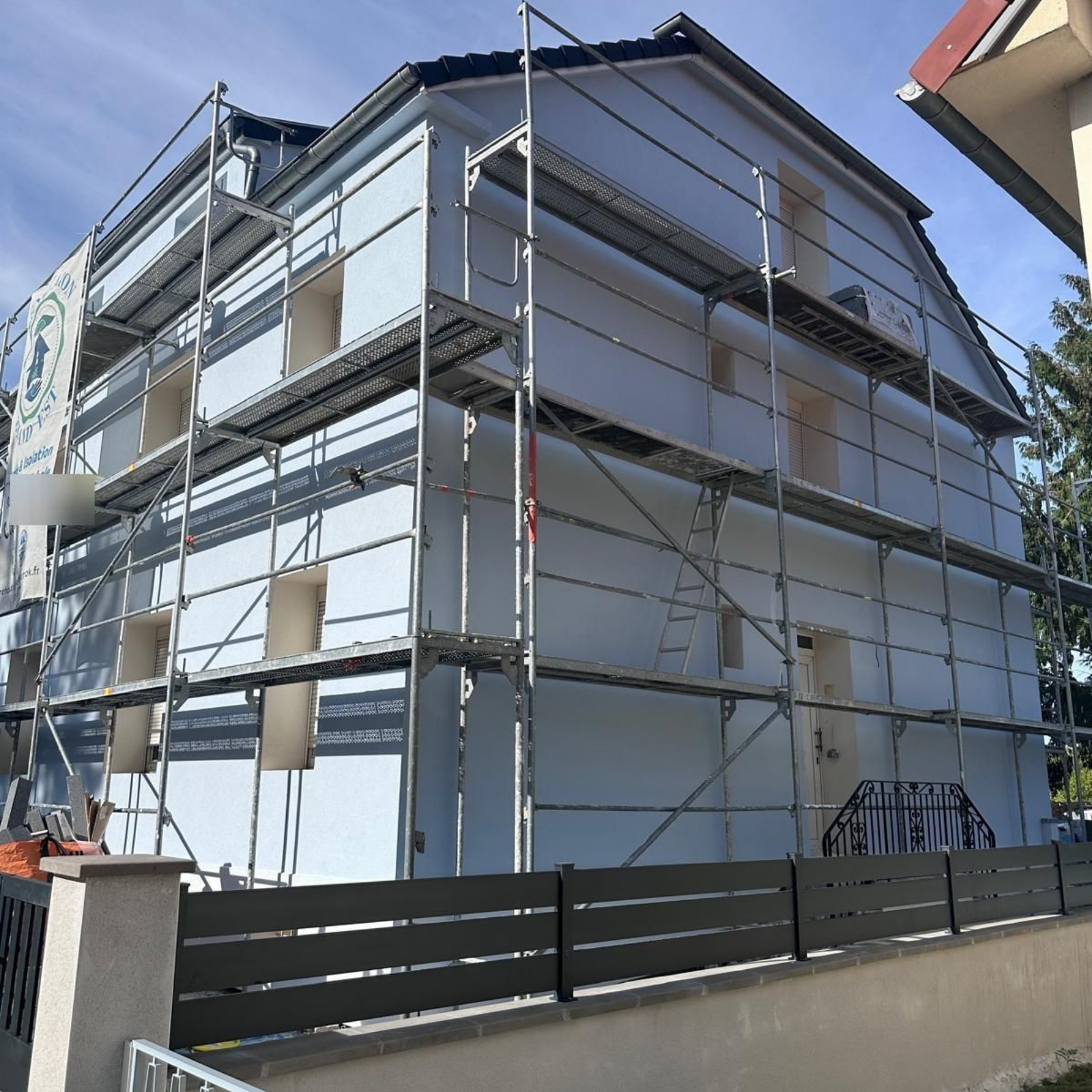 Extérieur du bâtiment en construction, recouvert d'isolant blanc, avec échafaudage.
