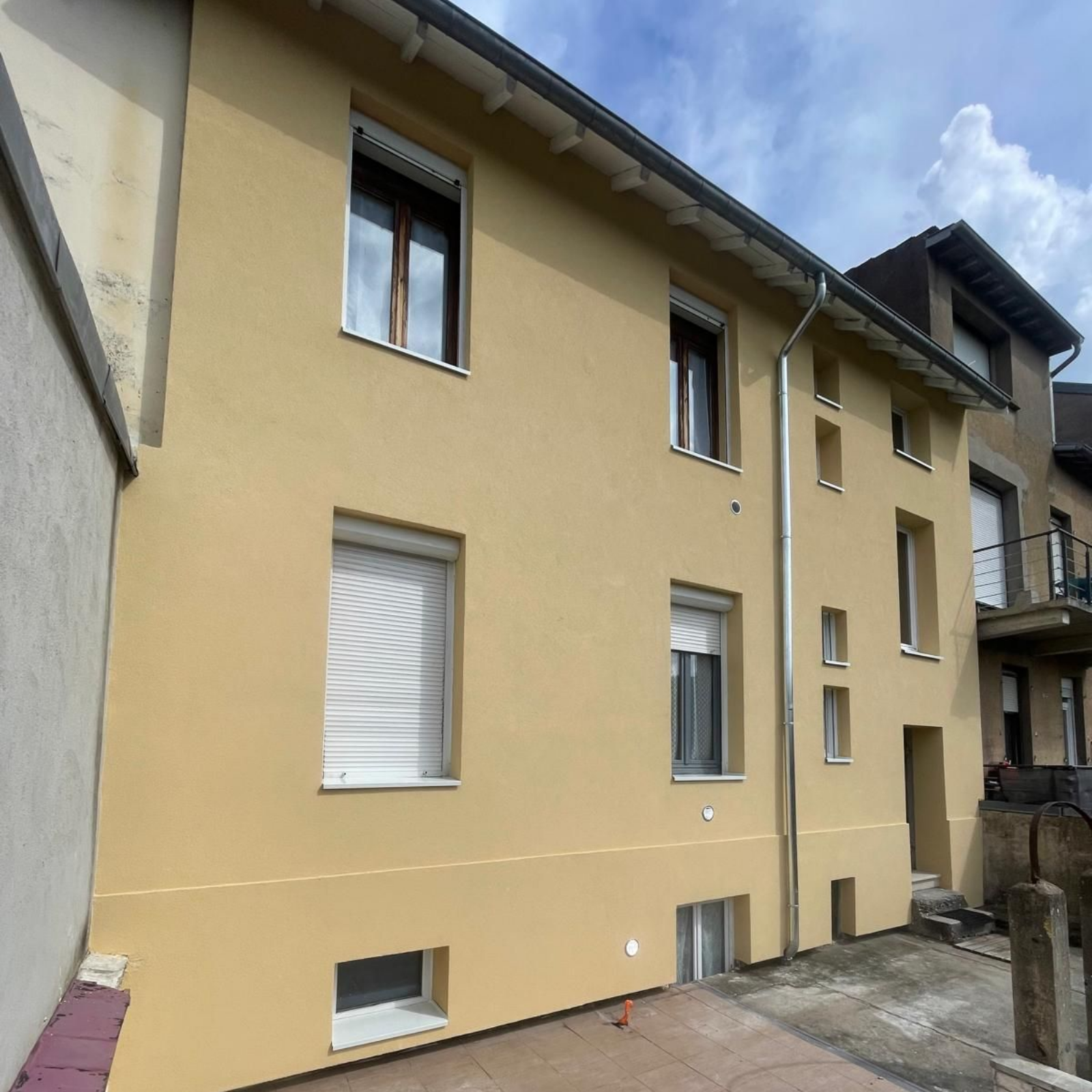 Bâtiment beige avec plusieurs fenêtres ; tuyau de drainage en métal sur le côté.