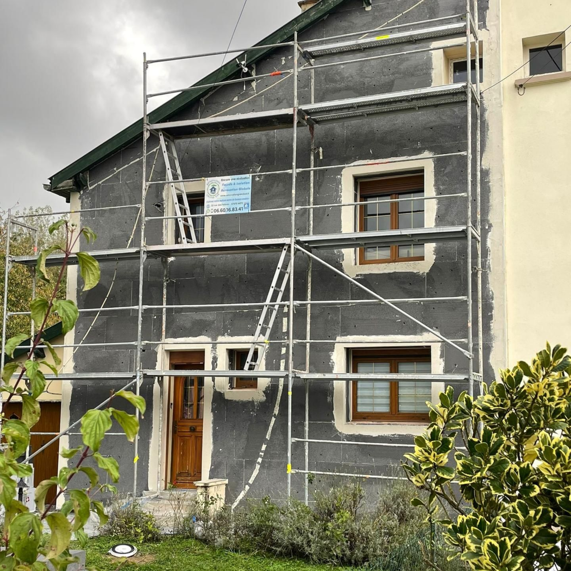 Extérieur de la maison en rénovation : échafaudages, isolation foncée, encadrements de portes et fenêtres marron.